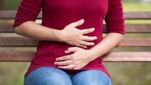 AN87 Bloating Hands Stomach 1296x728 header 300x169 - Woman Has Stomach Ache Sitting on Bench at Park