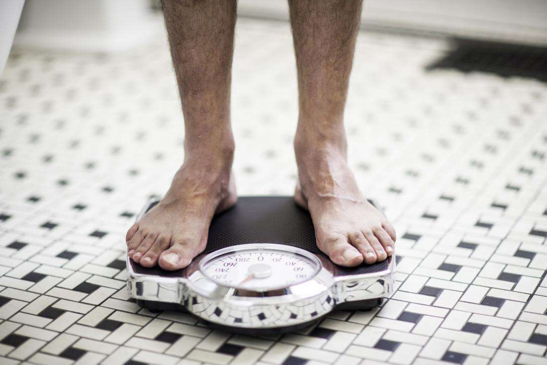 male feet standing on scales to check for weight loss alongside blood in the urine - چه چیزی باعث خون در ادرار مردان می شود ؟