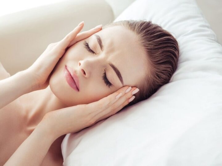 دختری که دراز کشیده است و دستان خودش را روی شقیقه هایش فشار می دهد